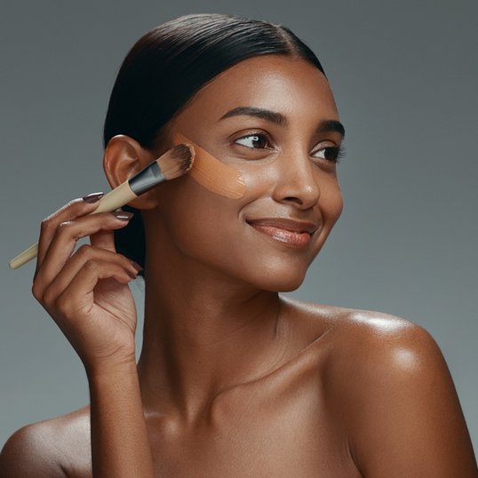 Mulher negra aplicando base para pele mista no rosto.