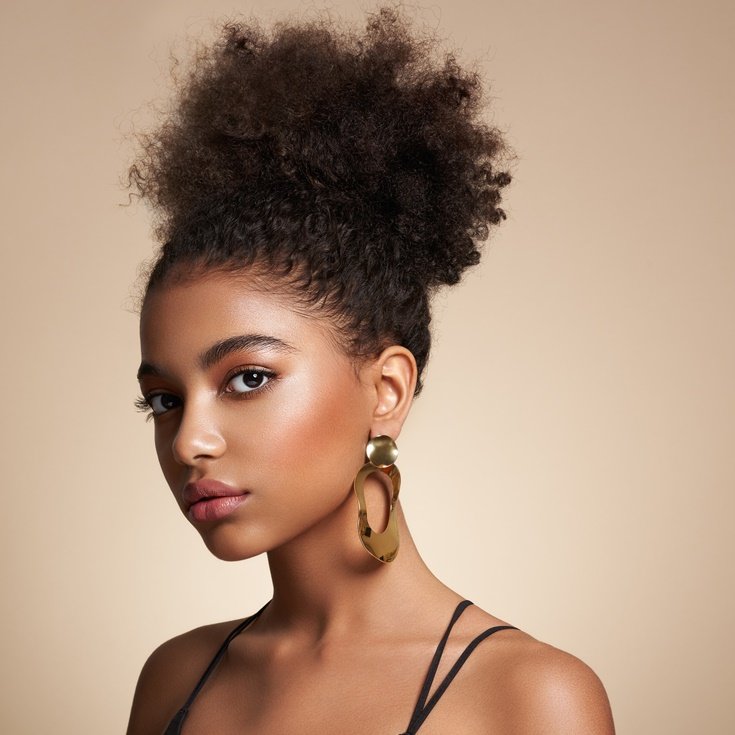 Menina negra usando maquiagem para fotos de formatura em fundo bege.