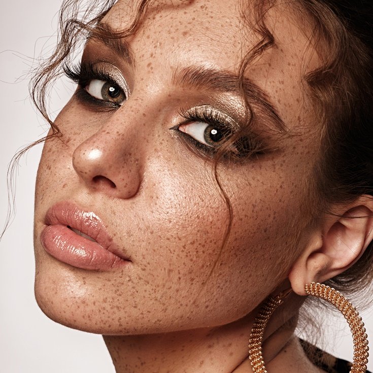 Close-up de maquiagem vibrante para o ano novo com sombra dourada e glitter nos olhos, lábios glossy e brincos de argola, celebrando as cores do ano novo com glamour.