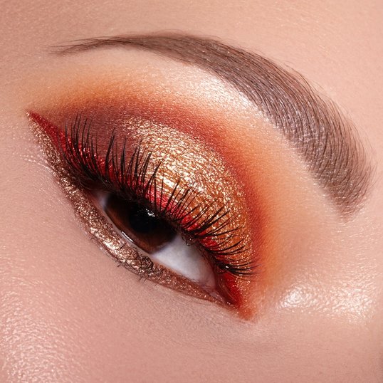 Close-up de maquiagem festiva para o ano novo, apresentando uma sombra amarela e brilhante na pálpebra, combinada com tons quentes de cobre e delineado vermelho sutil, realçando as cores do ano novo para um visual de prosperidade.
