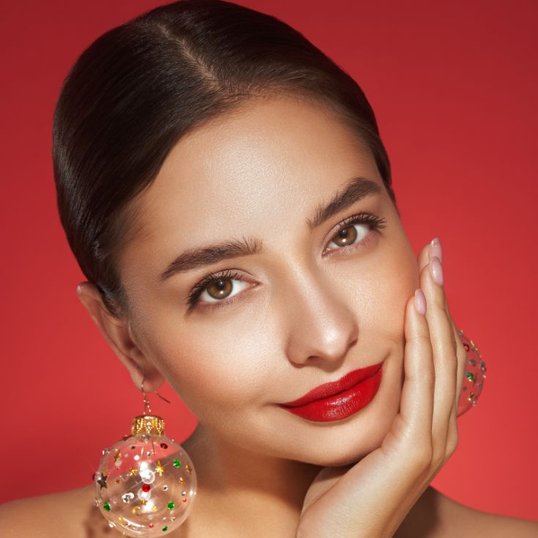 Modelo com brinco natalino,maquiagem clássica e batom vermelho em destaque.