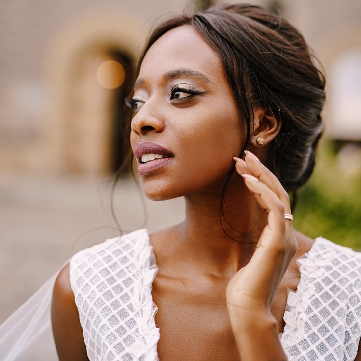 Mulher negra com a mão no rosto mostrando sua maquiagem de noiva no dia do seu casamento.