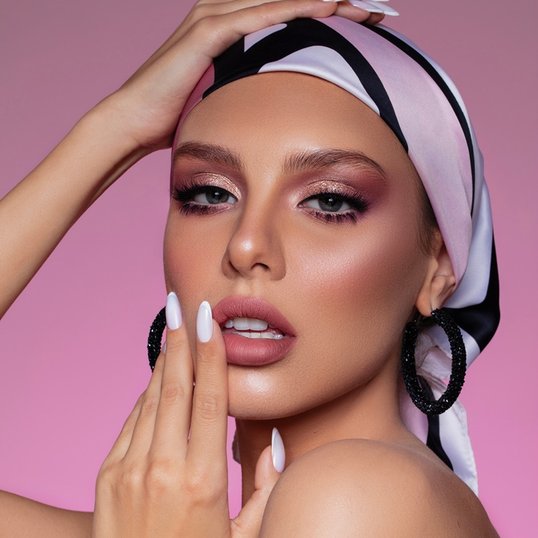 Close de uma mulher com um lenço na cabeça e maquiagem rosa, destacando os detalhes da maquiagem nos olhos e lábios.