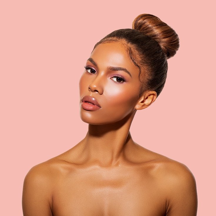 Mulher negra com cabelo castanho usando maquiagem soft glam em fundo rosa.