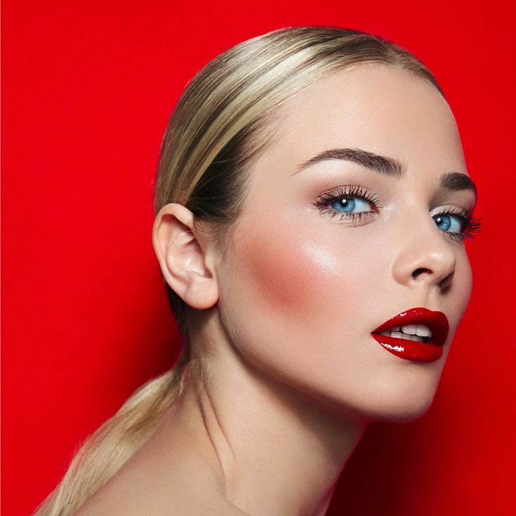 Mulher loira com olhos azuis usando batom vermelho intenso brilhante nos lábios.