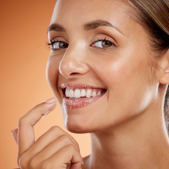 Mulher com olhos verdes e cabelo em um rabo de cavalo sorrindo enquanto esfolia os lábios.