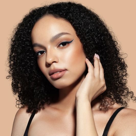 Mulher tocando a mão em seu cabelo enquanto usa delineado nos olhos e batom nude nos lábios.