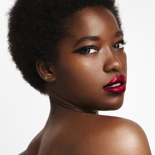 Mulher com maquiagem preta nos olhos e batom metálico vermelho nos lábios.