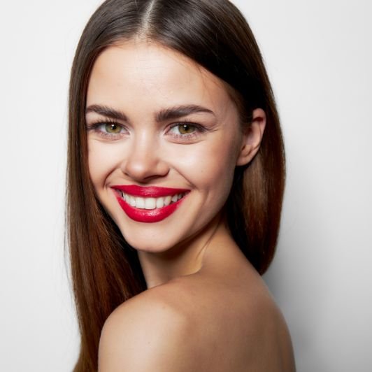 Mulher sorridente com cabelo castanho, olhos verdes e batom vermelho nos lábios.