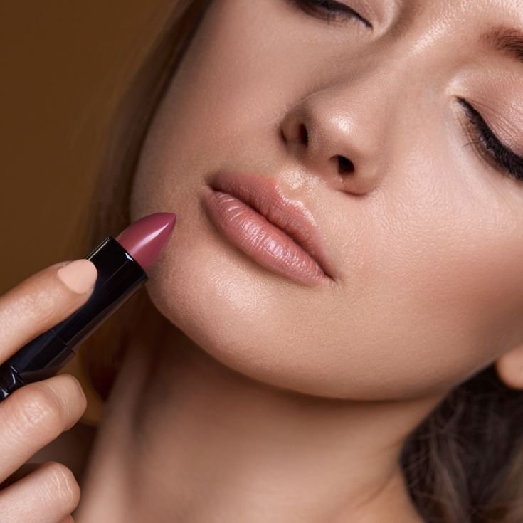 Mulher aplicando batom nude nos lábios.
