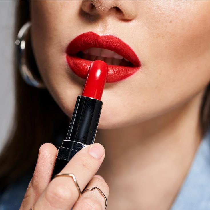 Mulher caucasiana aplica batom vermelho em seus lábios