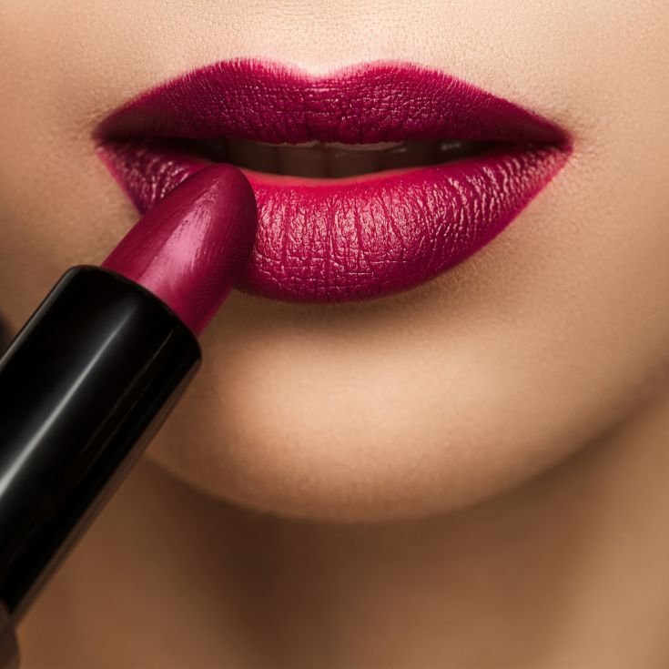 Mulher aplica batom vermelho vinho em seus lábios