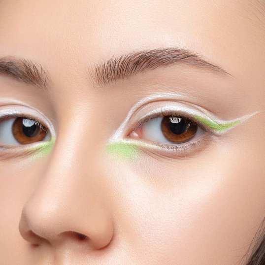 Mulher com delineador gráfico branco e verde nos olhos.