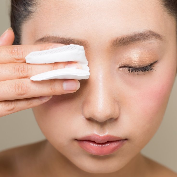 Mulher asiática removendo o rímel de seus olhos com algodão.