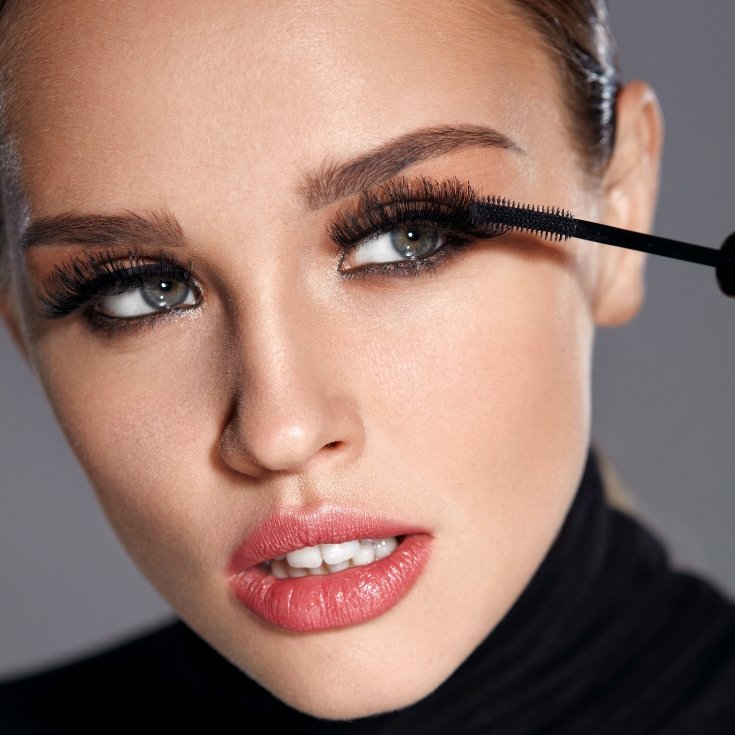 Mulher com boca entreaberta aplicando rímel nos seus cílios