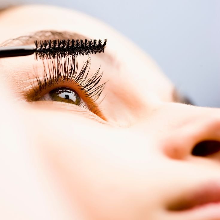 Mulher aplicando rimel nos seus olhos enquanto olha pra frente.