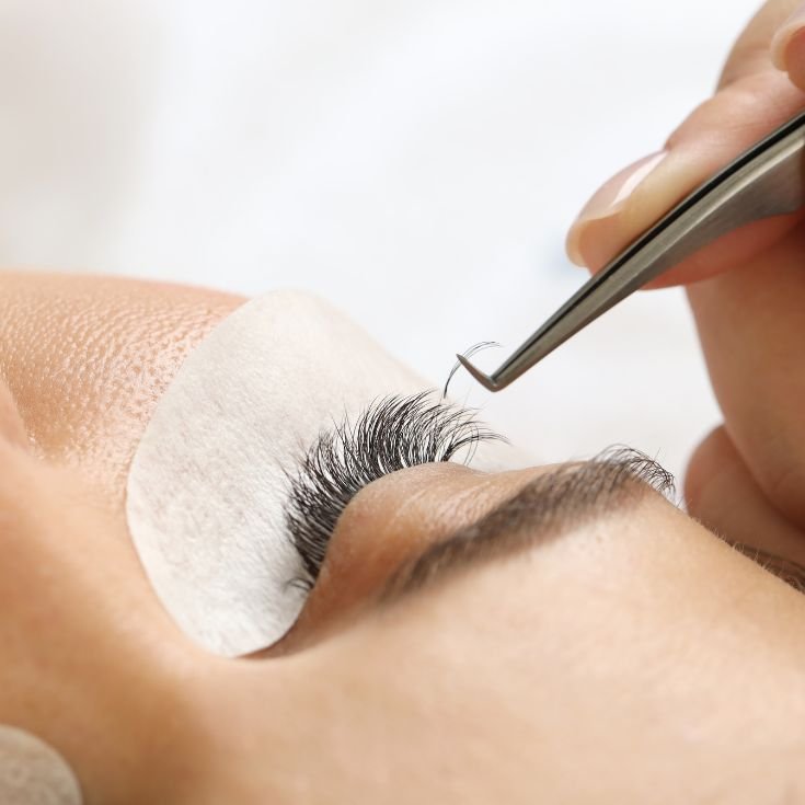 Mulher aplicando cílios fio a fio em sua cliente com unha quadrada.