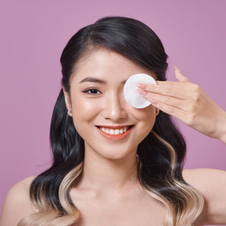 Mulher com traços asiáticos demonstra como remover o rímel à prova d’água.