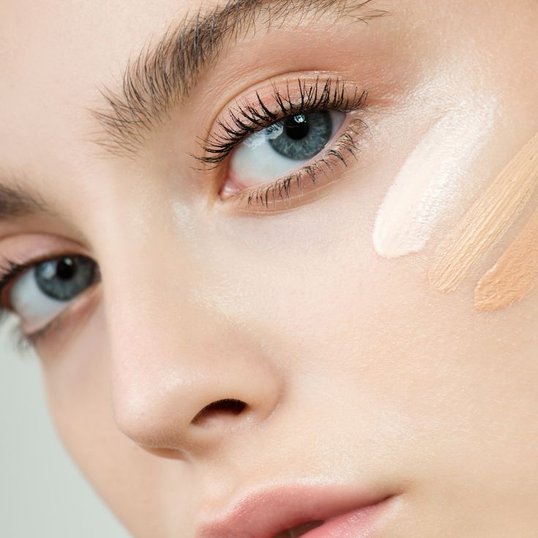 Mulher olhando para a câmera com olhos azuis e três cores de base no seu rosto.