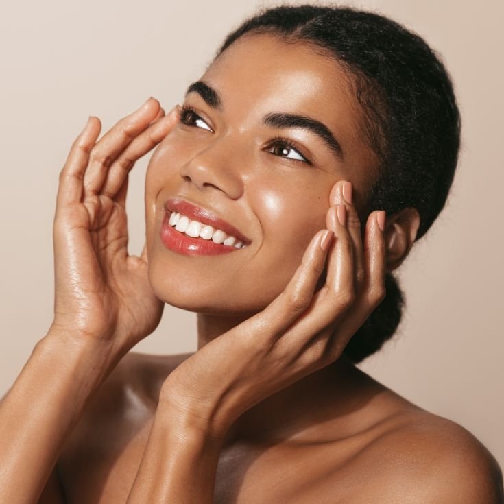 Mulher jovem de pele negra sorrindo, com rosto iluminado, viçoso e aparência saudável, evidenciando o efeito glass skin. A maquiagem é leve, com brilho natural na pele.