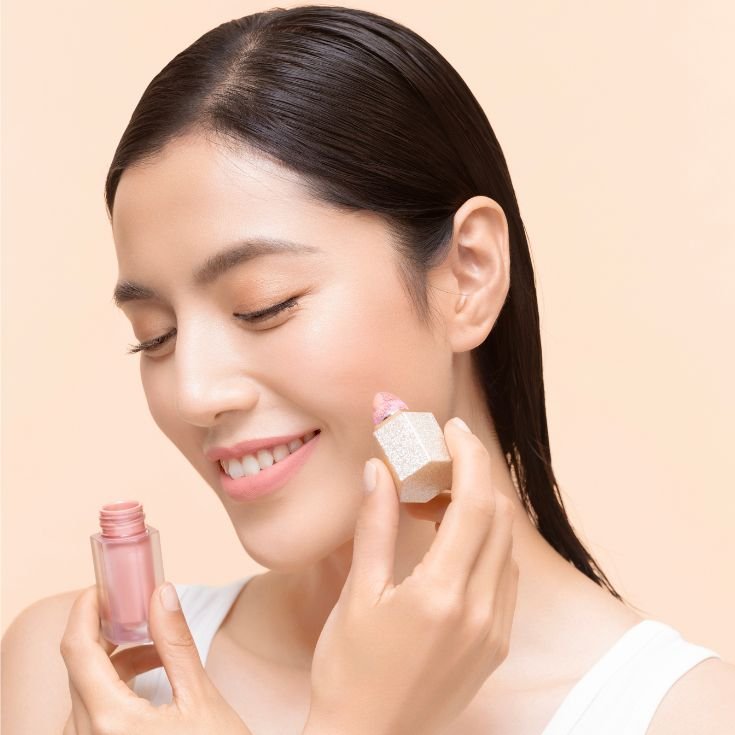 Mulher aplicando blush líquido claro no rosto.