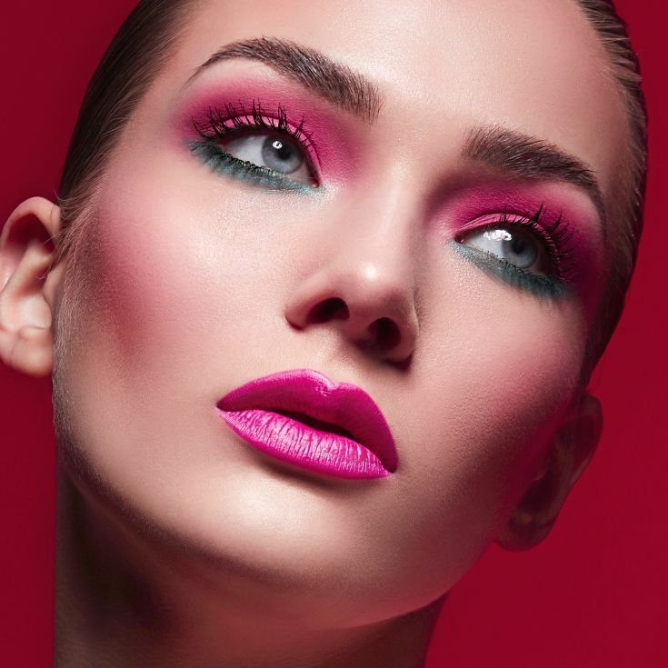 Mulher com sombra rosa na pálpebra móvel e azul embaixo dos olhos enquanto usa blush rosa nas bochechas e batom rosa pink nos lábios.