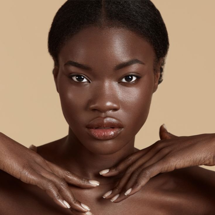 Mulher com rosto oval e mãos sobrepostas no seu ombro. Sua pele está com aspecto natural e com pontos iluminados.