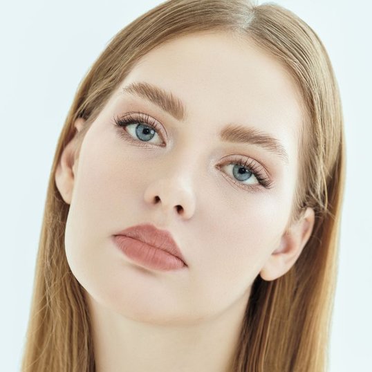 Mulher com rosto triangular, cabelos loiros, olhos azuis e boca com tom terroso.