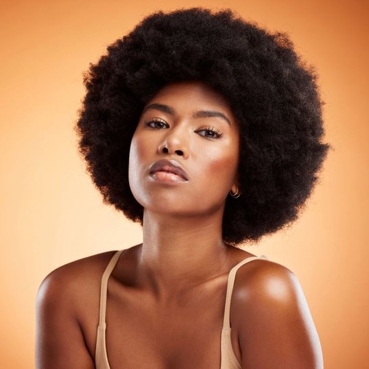 Mulher com cabelo cacheado curto e maquiagem com blush marrom nas bochechas.