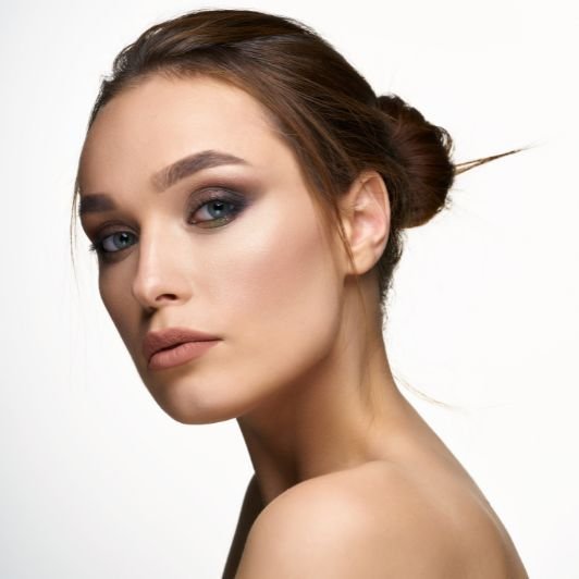 Mulher com coque no cabelo liso e maquiagem com olho esfumado e blush marrom acinzentado nas bochechas.