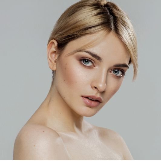Mulher loira com cabelo curto e maquiagem leve com blush marrom médio nas bochechas.
