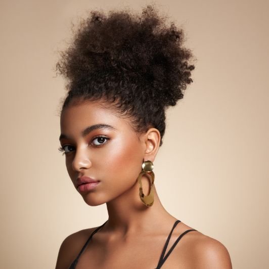 Mulher com cabelo cacheado em coque e maquiagem com blush marrom nas bochechas.
