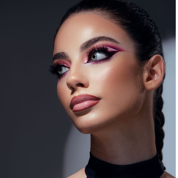 Mulher com sombra rosa e delineador preto nos olhos, lip combo nude nos lábios e blush marrom terroso nas bochechas.