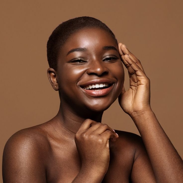 Mulher sorridente com a mão no rosto mostrando pele luminosa e saudável.