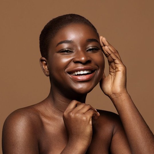 Mulher sorridente com a mão no rosto mostrando pele luminosa e saudável.