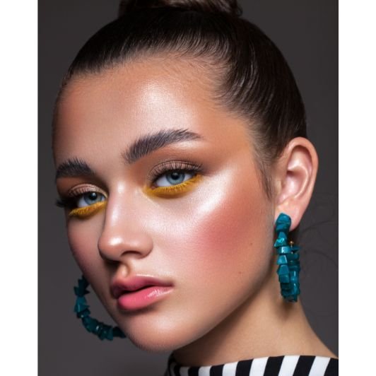 Menina com sombra marrom na pálpebra móvel e sombra amarela na parte inferior dos olhos usando iluminador liquido perolado nas bochechas.
