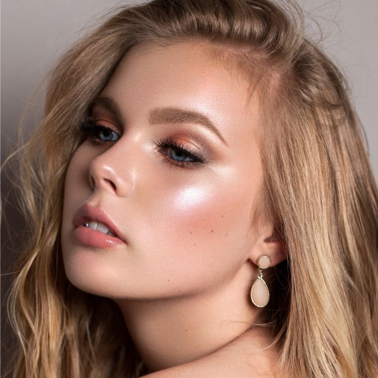 Mulher loira usando maquiagem colorida nos olhos e iluminador liquido rosado nas bochechas