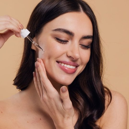 Mulher sorridente passando sérum facial com vitamina E no rosto.