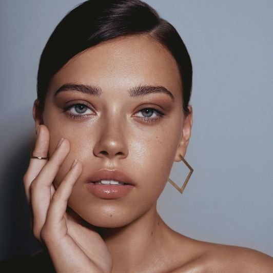 Mulher com mão no queixo e sombra marrom na pálpebra com maquiagem simples no dia.