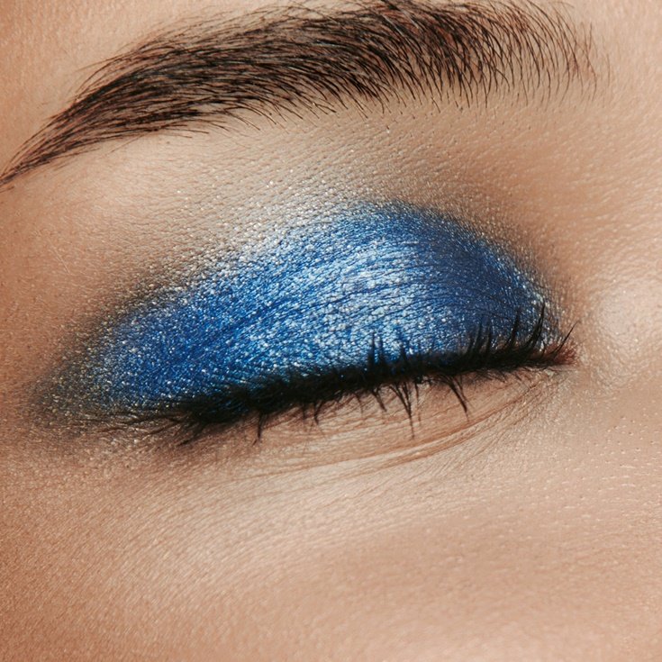 Close-up da pálpebra com a sombra colorida em tons de azul vibrante. A sombra se estende do canto interno ao externo do olho, criando um visual marcante.