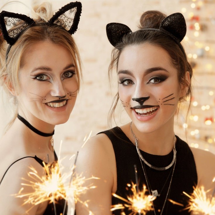Duas mulheres com maquiagem de gatinha para o Carnaval, usando orelhas de gato e bigodes desenhados.