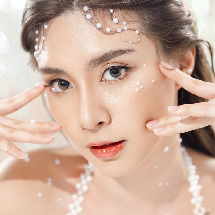 Close-up de uma mulher com maquiagem de Carnaval delicada, usando pérolas no rosto e um colar de pérolas, criando um look elegante.