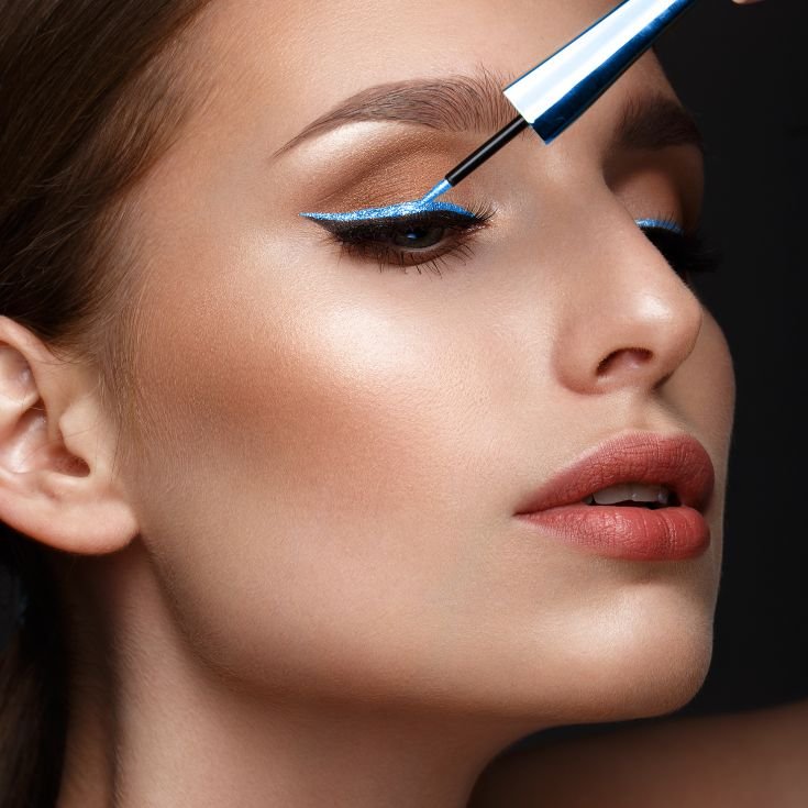 Mulher aplicando delineador azul com a mão enquanto olha para o lado direito.