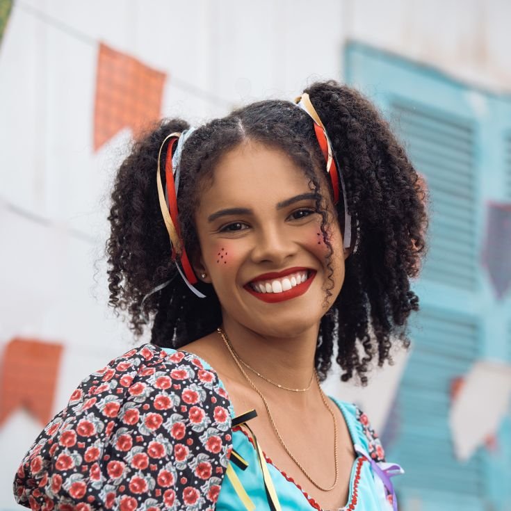 Mulher usando roupa típica de festa junina com fitas no cabelo e maquiagem com sardinhas e blush marcado com batom vermelho.