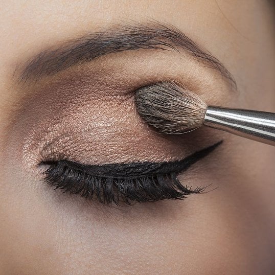Mulher aplica sombra nos olhos para finalizar sua maquiagem com batom vermelho