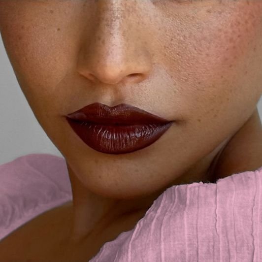Mulher de pele morena utilizando um batom vermelho escuro terroso em sua maquiagem.