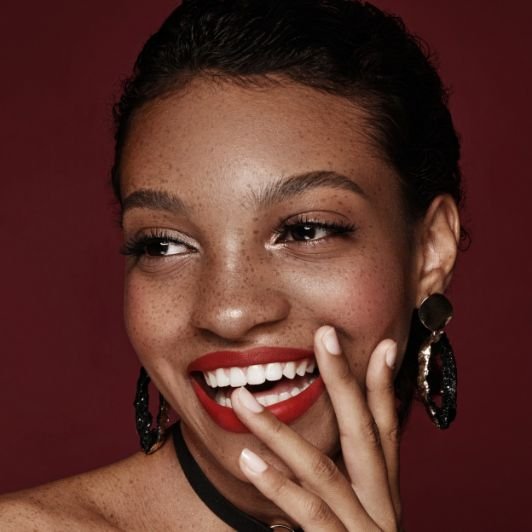 Mulher com a pele negra usando um batom vermelho escuro em sua maquiagem.