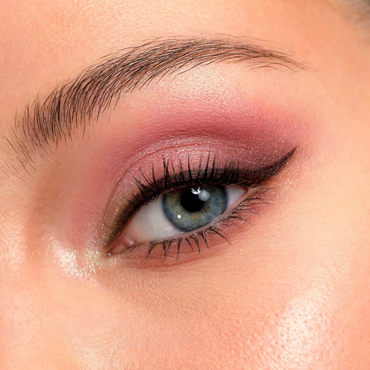 Mulher de olhos azuis com uma sombra rosa esfumada no côncavo e pálpebra móvel finalizado com um delineado gatinho.