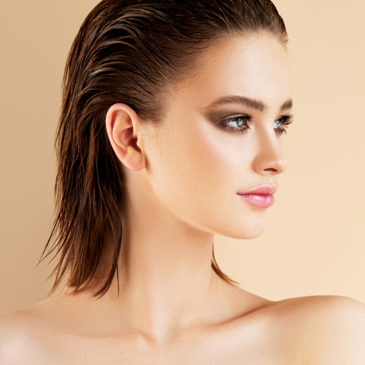 Mulher com o cabelo em um aspecto molhado com maquiagem preta esfumada em um fundo bege.