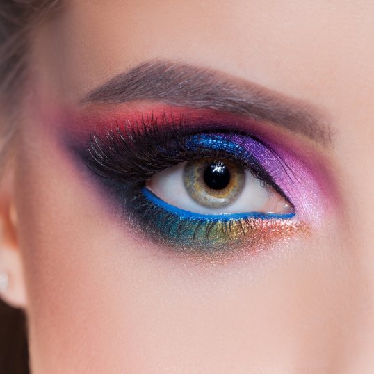 Maquiagem com sombras coloridas e lápis de olho azul na linha d’água.